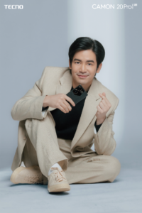 Joshua Garcia in a brown suit sitting with a black tecno CAMON 20 Pro